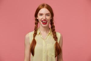 Indoor portrait of young ginger female with freckles posing over pink background photo