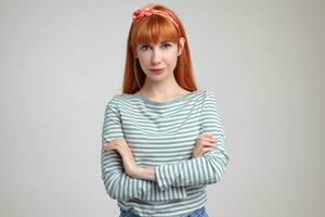 Indoor portrait of young ginger female posing over white wall looking into camera with calm facial expression photo