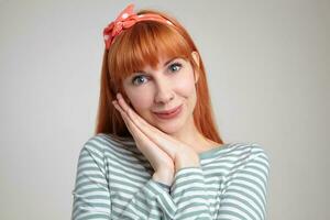 Indoor portrait of young ginger female posing over white wall looking into camera with happy facial expression photo