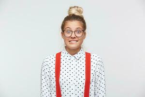 temeroso joven hembra con rubia pelo vestido en blanco camisa, rojo tirantes, teniendo confuso culpable mirar, mordiendo su inferior labio, sensación lo siento para haciendo alguna cosa incorrecto y haciendo terrible Error foto