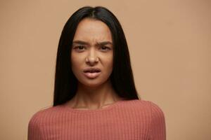 Portrait of an upset unsatisfied asian woman. Young caucasian girl isolated over beige background looks skeptic and nervous, disapproving expression on face, negative emotion photo