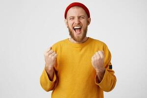 Cheerful young attractive man celebrating his success. Close up of young bearded male screaming of victory and raised fists up. Isolated white background photo