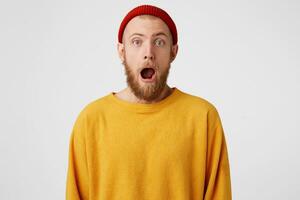 Young attractive blue-eyed man with a beard looks surprised shocked stunned frightened wide open mouth jaw lowered. Guy in shock from what he saw,stands and can't budge,isolated on white background. photo