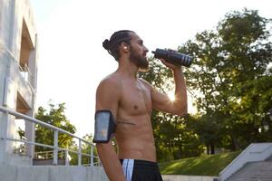 retrato de joven hermoso barbado joven hombre después trotar en el parque, Bebiendo agua. Guías sano activo estilo de vida. aptitud masculino modelo. foto