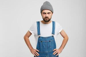 hombre con un barba furioso. enojado serio decisivo, en pie en un actitud Listo a Rápido su negativo actitud, manos sostener en su caderas, Cejas frunció el ceño. foto