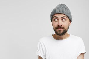 Close up of a young man in a gray hat curiously, with interest glances, looks to the left, on the side of him there is an empty copy space for your text or advertisement photo