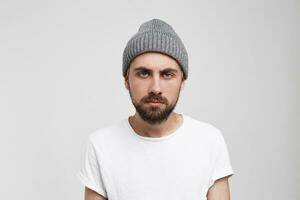 Tired guy with a facial expression without distinction, apathy and fatigue,detachment without a gleam in his eyes, a little stoop looks straight into the camera, wearing a white T-shirt and a gray hat photo