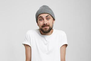 Guilty and confused young man shrugging shoulders, making helpless gesture with hands, having Oops expression on his face. Feeling sorry for doing something wrong,over white background photo