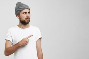 An unshaven man with a beard in a gray hat shows his index finger to the right looking away to the empty copy space, looks incredulous disgruntled wary photo
