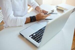 Cropped shot of businessman wears white shirt using laptop, notebook and smartphone sitting at the table in office photo