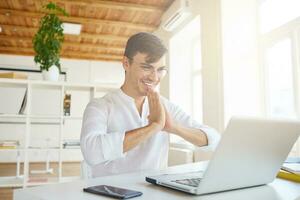 Closeup of smiling handsome young businessman wears white shirt and glasses using laptop and cell phone feels happy and working at the table in office photo