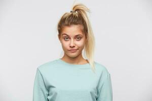 Portrait of sad pretty young woman with blonde hair and ponytail wears blue sweatshirt shows feels upset and depressed isolated over white background photo