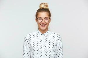 Closeup of smiling pretty young woman with bun wears polka dot shirt and glasses feels happy and confident isolated over white background photo