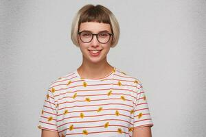 Closeup of smiling pretty young woman wears striped t shirt and spectacles feels confident and looks directly in camera isolated over white background photo