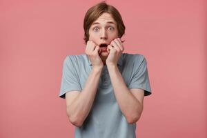 Portrait of scared teen in panic nervous excited mouth opened in fear dressed in polo t-shirt keeps palm on face, feels himself frightened, isolated on pink background with copy space photo