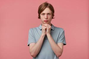 Gloomy sad guy looks hopelessly rests his chin on folded hands into a fist, isolated on a pink background.The boy needs strength and motivation for further struggle lacking self-confidence. photo