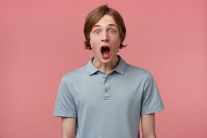 Surprised male, keeps mouth open, being stunned, receives positive unexpected news, isolated over pink background. Omg concept. Horizontal shot of shocked young male, expresses great surprisment. photo