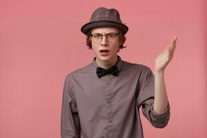 Unsatisfied serious young smartly dressed guy holding hand up looking camera through glasses moralizing, defends his point of view, makes moral lecture, over pink background photo