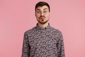 Sweet kiss directly to the camera. Portrait of pleasant nice guy in glasses sending air kiss with pout lips isolated on pink background, shows tender feelings photo