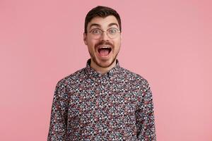 Excited man popping eyes and shouts loudly. Surprised male, keeps mouth open, being stunned, over pink background. Horizontal shot of shocked young male filled with emotion photo