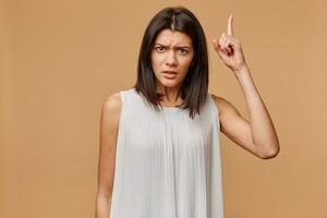 Attention, listen to me. Close up portrait of young woman wagging her finger isolated beige wall background. Negative human emotions face expression, life perception, feelings, body language, attitude photo