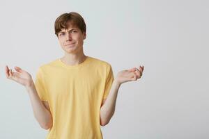 Portrait of confused upset young man wears yellow t shirt feels embarrassed and holding copyspace at both palms isolated over white background photo