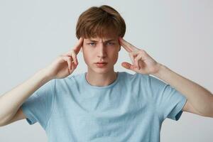 Closeup of pensive tensed young man wears blue t shirt touching his temples, thinking and having a headache isolated over white background photo