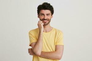 Closeup of cheerful attractive bearded young man wears yellow t shirt looks confident and keeps hands folded isolated over white background photo