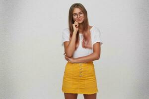 Portrait of happy beautiful young woman wears t shirt, yellow skirt and glasses standing and keeps hands folded isolated over white background photo