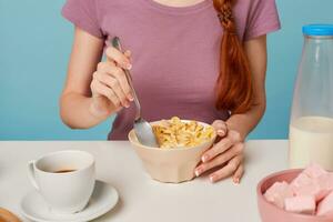 Close up of girl hands sitting at the table is going to have breakfast, pour milk into a plate with mussels and mixing spoon. Isolated on a blue background. photo