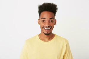 Portrait of cheerful amazed african american young man with curly hair wears yellow t shirt looks excited and smiling isolated over white background photo