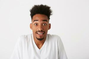 Portrait of shocked confused african american young man with curly hair wears t shirt looks embarrassed and shrugging his shoulders isolated over white background photo