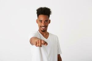 Closeup of cheerful handsome african american young man with curly hair wears t shirt looks happy and points at camera isolated over white background photo