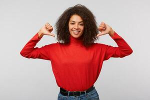 Close up photo of amazing beautiful african american lady with thumbs fingers pointing herself saying I love myself I am best. Wearing red longsleeve sweater isolated white background