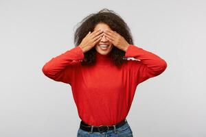 Happy african american mother counting to ten while playing hide and seek with children. Portrait of charming playful mom with afro hairstyle covering eyes with palms and smiling broadly from joy photo