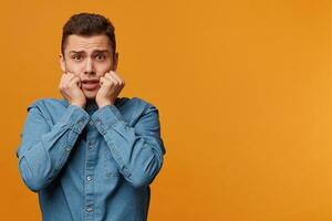 Headshot of hysterical student guy looking in despair and panic, nervous, worried about the exam results, keeps fists near his face,isolated over yellow background, with copy space for your text photo