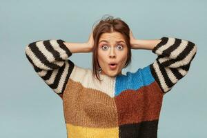 Frightened woman grabbed her head. Surprised female, keeps mouth open, being stunned,over blue background.Horizontal shot of shocked young female, expresses great surprisment, catastrophe had happened photo