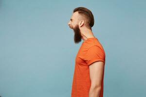 Man standing profile sideways shouts loudly, facial expression of anger, isolated over blue background photo