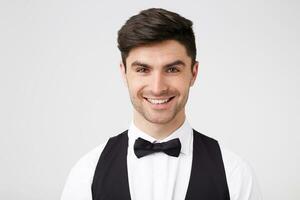 bonito atractivo chico inteligentemente vestido con negro corbata de moño mirando Derecho a el cámara con un amplio alegre sonrisa, mira contento contento, aislado en blanco antecedentes foto