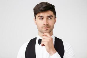 Portrait of thoughtful young man holding hand on chin and looking away standing isolated over white background. Copy space for advertisement.Ponders the idea, doubts, weighs possible options photo