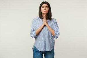 Sad upset woman folded hands in praying gesture and looks camera with hope, prays for close person, wants something, needs another chance, hopes for luck, over white background photo