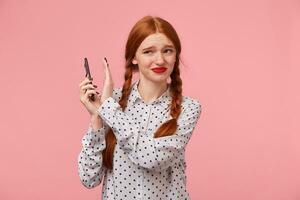 Girl with red braids keeps the phone at a distance from, fences off with hand from it, frowns at the fact that the other person shouts, swears, an unpleasant telephone conversation, a quarrel. photo