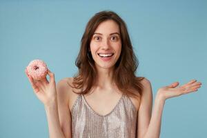 joven europeo mujer yendo a comer dulce rosado rosquilla sostiene eso en mano, terminado aislado azul fondo, asombrado, muy entusiasmado, aplausos contento emoción foto