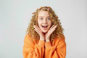 Lovely tender nice girl looks amazed surprised, keeps palms near face as if demonstrates it or tries to pay attention, dressed in oversized sweatshirt. People, body language and facial expressions photo