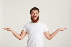 Closeup of cheerful attractive young man hipster with beard wears t shirt feels happy and holding copyspace at both palms isolated over white background photo