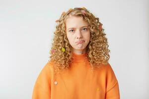 Close up of emotional girl looks sad, upset, frustrated, displeased, expresses offense,crying, lower lip pouted, showing defenseless, wears orange sweatshirt, stands isolated over white background. photo