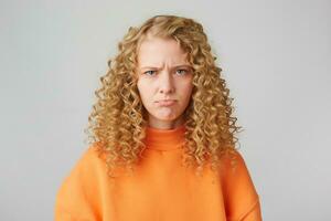 Portrait of emotional angry grumpy girl looks sad, upset, frustrated, displeased, expresses insult,lower lip pouted, wears orange sweatshirt, stands isolated over white background. photo