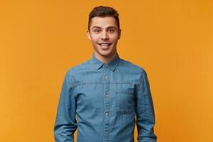 atractivo joven encantador chico sonrisas amablemente, muestra su sano dientes, vestido en un nuevo mezclilla camisa, aislado terminado amarillo fondo.a estudiante es teniendo divertido chateando con su amigos. foto