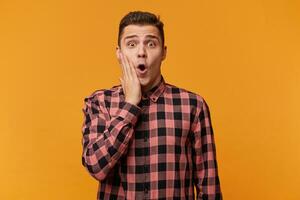 Photo of stunned attractive guy looks with unexpected expression directly at camera, being shocked to recieve increadable news, isolated over yellow background. People, emotions, reaction