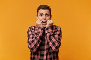 Portrait of hysterical student guy looking in despair and panic, nervous on test, worried about the exam results, not knowing what to answer, hands near mouth, mouth opened in a shout photo